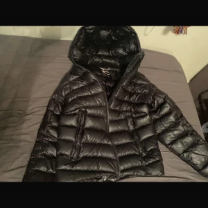 Svart dunjacka från Colmar - Säljer en snygg svart dunjacka från Colmar i mycket bra skick. Jackan har en quiltad design med dragkedja och en praktisk huva. Perfekt för kalla vinterdagar och håller dig varm och stilren. Passar bra till både vardag och lite finare tillfällen. Köpt förra vinter, inga defekter