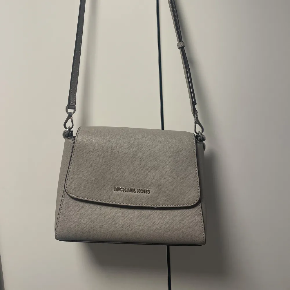 Säljer en stilren grå axelväska från Michael Kors i mycket bra skick. Väskan har en justerbar axelrem och ett snyggt, strukturerat material. Knappt använd då jag mest använder guldsmycken vilket gör att den inte passar till. Köpt i USA i Michael Kors egna butik . Laukut & Käsilaukut.