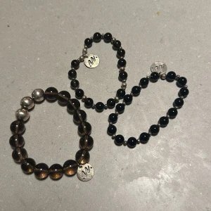 Svarta och bruna armband med pärlor - Tre stilrena armband med svarta och bruna pärlor. Varje armband har en liten metallbricka med en ingraverad bokstav. Perfekta för att ge en elegant touch till din outfit. Passar både till vardag och fest!