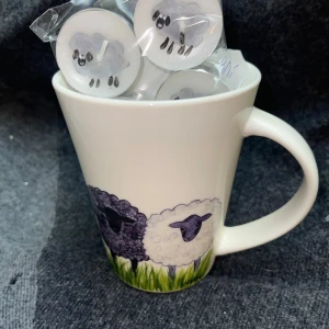Vit mugg med fårmotiv - Charmig vit mugg med söta fårmotiv i olika färger. Perfekt för en mysig kopp te eller kaffe. Muggen har ett bekvämt handtag och är dekorerad med grönt gräs vid basen. En rolig och unik design som passar perfekt för djurälskare eller som en present. Plus motivet på värmeljus flyter med 