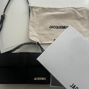 Svart axelväska från Jacquemus - Säljer en elegant svart axelväska från Jacquemus i nytt skick. Väskan är tillverkad i skinn och har en stilren design med ett justerbart axelband. Perfekt för både vardag och fest! Kommer med originalförpackning och dustbag. 