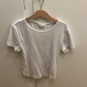Vit kortärmad topp från Gina Tricot - Säljer en enkel och stilren vit kortärmad topp från Gina Tricot i storlek XS. Perfekt basplagg för sommaren, gjord i mjukt bomullsmaterial. Toppen har en rund halsringning och är i mycket bra skick. Passar till allt från jeans till kjol!