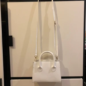 Vit axelremsväska från Shein - Säljer en stilren vit axelväska i syntetmaterial. Väskan har både handtag och en justerbar axelrem, vilket gör den perfekt för både vardag och fest. Insidan är rymlig nog för dina nödvändigheter. Den är i mycket bra skick och redo för en ny ägare!