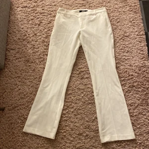 Vita kostymbyxor - Säljer ett par eleganta vita kostymbyxor i mycket bra skick. De har en klassisk bootcut passform och är perfekta för både formella och semi-formella tillfällen. Byxorna är lågmidjade och tillverkade i ett bekvämt material som ger en stilren look. 