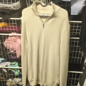 Beige stickad tröja från Zara - Säljer en snygg beige stickad tröja från Zara i mycket bra skick. Den har en dragkedja vid halsen och är perfekt för både höst och vinter. Tröjan är långärmad och har en ribbad struktur som ger en stilren look. Perfekt för att hålla sig varm och trendig!