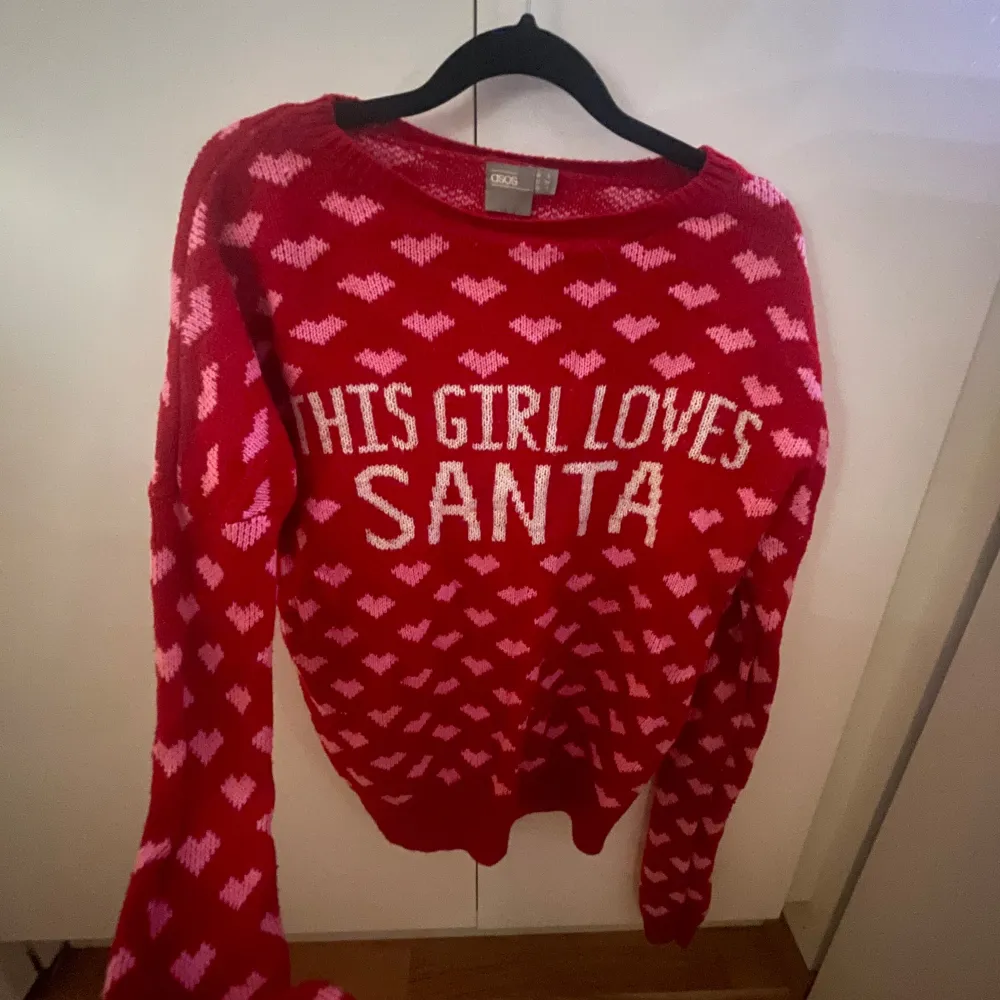 Superfin röd stickad tröja från ASOS med texten 'This Girl Loves Santa' i vitt. Den har ett gulligt hjärtmönster i rosa över hela tröjan. Perfekt för jul och vinterns mysiga stunder. Långärmad och riktigt bekväm att ha på sig. Perfekt för att sprida julstämning! 🎅❤️. Stickat.