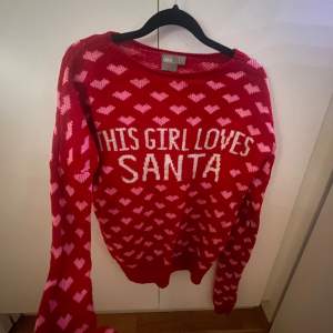 Superfin röd stickad tröja från ASOS med texten 'This Girl Loves Santa' i vitt. Den har ett gulligt hjärtmönster i rosa över hela tröjan. Perfekt för jul och vinterns mysiga stunder. Långärmad och riktigt bekväm att ha på sig. Perfekt för att sprida julstämning! 🎅❤️