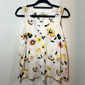 Blommig ärmlös topp från Carin Wester - Säljer en superfin ärmlös topp från Carin Wester. Den är vit med ett färgglatt blommönster i gult, rosa och svart. Toppen har en lös passform och är gjord i ett mjukt material.