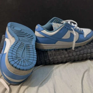 Nike Dunk i blått och vitt - Säljer ett par Nike Dunk i blått och vitt. Skorna har en klassisk design med snörning och är i mycket bra skick. Perfekta för både vardag och träning. Storlek är inte specificerad, men de ser ut att passa en normal passform.