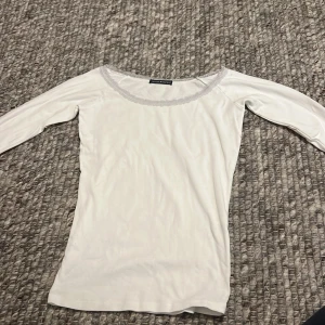 Vit topp från Brandy Melville - Säljer en superfin vit topp från Brandy Melville. Den har en söt spetsdetalj runt halsringningen och är i ett mjukt material. Perfekt för både vardag och fest! Passar till allt och är i mycket bra skick.