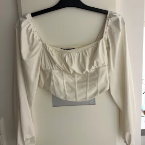 Vit korsettblus med långa ärmar - Säljer en superfin vit korsettblus med långa ärmar. Den har en elegant och romantisk stil med en åtsittande passform i midjan. Perfekt för både fest och vardag! 💫