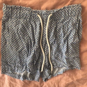 Blåmönstrade shorts med snörning - Säljer ett par blåmönstrade shorts med vita detaljer och snörning i midjan. Perfekta för sommardagar eller en avslappnad dag hemma. De har en lös passform och är superbekväma. Mönstret är smått och ger en stilren look💕