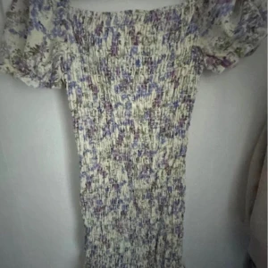 Blommig klänning med puffärmar - Säljer en superfin blommig klänning med puffärmar. Den har en smockad design som ger en tight passform. Klänningen är i en ljus färg med lila och gröna blommor. Perfekt för en romantisk look!