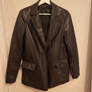 Brun skinnjacka från New Look - Snygg brun skinnkavaj från New Look i storlek s. Jackan har en klassisk kavajstil med knappar och långa ärmar. Den är i mycket bra skick och ger en cool look till vilken outfit som helst.