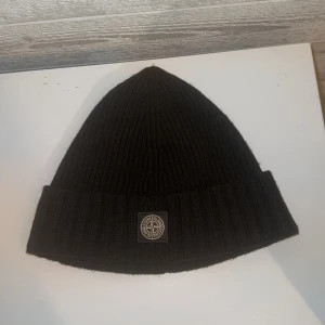 Svart ribbad mössa från Stone Island - Säljer en snygg svart ribbad mössa från Stone Island Junior. Storleken är junior 3 och är den största junior storleken som finns. Mössan passar mig i storlek och jag är en 19 åring kille med normal stort huvud