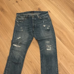 Blå jeans från Polo Ralph Lauren - Snygga blå jeans från Polo Ralph Lauren med slitna detaljer och en klassisk femficksdesign. Jeansen har en rak passform och är tillverkade i denim. Perfekta för en avslappnad stil. Nypris ca 3000