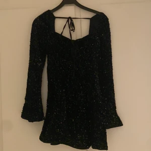 Svart glittrig klänning med paljetter - Snygg svart klänning med glittriga paljetter och knytning fram. Den har långa ärmar och en kort längd, perfekt för en festlig kväll. Materialet ger en lyxig känsla och den sitter bekvämt på kroppen aldrig använd på grund av liten för mig 🥰