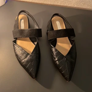 Svarta spetsiga ballerinaskor med rem - Snygga svarta ballerinaskor från Pieces med spetsig tå och krokodilmönster. Skorna har en bred rem över foten i mocka som ger en elegant touch. Perfekta för en stilren look. 🖤