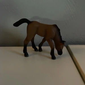 Leksaks häst - En brun hästfigur med svarta ben och svans. Hästen står i en böjd position med huvudet nedåt. Perfekt för samlare eller som dekoration.
