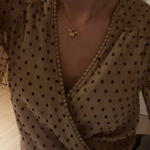 Beige omlottblus med prickar - Säljer en söt beige omlottblus med svarta prickar. Blusen har trekvartsärmar och en knytning i midjan som ger en fin passform. Perfekt för en stilren och chic look.