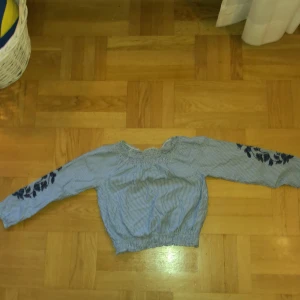 Blå- och vitrandig tröja från KappAhl - Säljer en söt blå- och vitrandig tröja från KappAhl med blommiga broderier på ärmarna. Tröjan har långa ärmar och en elastisk nederkant som ger en bekväm passform. Perfekt för en stilren och avslappnad look. 🌸