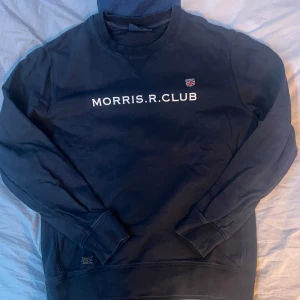 Mörkblå tröja från Morris R. Club - Säljer en stilren mörkblå tröja från Morris R. Club med text på bröstet. Tröjan har långa ärmar och en klassisk rund halsringning. Perfekt för en avslappnad och snygg look. Storlek: Medium. Hör av dig vid några frågor.😊