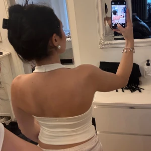 Vit ärmlös halterneck topp - Säljer en vit halterneck topp med v-ringning. Toppen är ärmlös. Materialet är mjukt och bekvämt. 