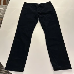 Svarta manchesterbyxor från NN07 - Snygga svarta manchesterbyxor från NN07 i modellen Karl. Byxorna är tillverkade i 98% bomull och 2% elastan för en bekväm passform. Perfekta för en stilren look.