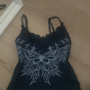 Mörkblå linnetopp  - Snygg mörkblå linnetopp med spetsdetaljer vid halsringningen och ett coolt tryck av en fjäril och stjärnor. Perfekt för en unik och stilren look.