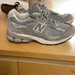 Grå sneakers från New Balance - Snygga grå sneakers från New Balance med klassisk N-logga på sidan. Skorna har en bekväm sula och är tillverkade i en kombination av mocka och syntetmaterial. Perfekta för en avslappnad stil.