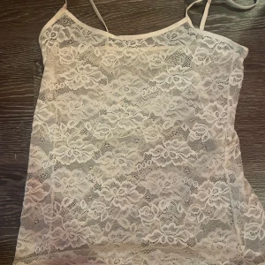 Vit spetslinne - Säljer ett vackert vitt spetslinne med tunna axelband. Perfekt för en somrig look eller som ett lager under andra plagg. Linnet har ett blommigt mönster och är tillverkat i ett lätt och luftigt material.
