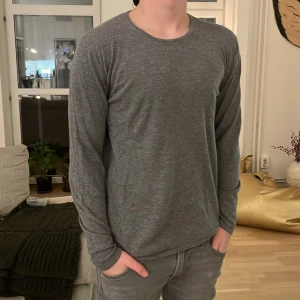 Grå långärmad tröja från Ljung - Säljer en stilren grå långärmad tröja från Ljung by Marcus Larsson. Perfekt för en avslappnad look med mjukt material och rund halsringning. Passar bra till jeans eller chinos för en enkel men snygg outfit.