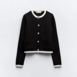 Svart kofta med vita detaljer från Zara - Snygg svart kofta från Zara med vita kanter och dekorativa knappar framtill. Den har långa ärmar och två fickor. Perfekt för en stilren look.