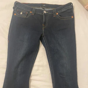 Mörkblå jeans från True Religion - Snygga mörkblå jeans från True Religion med låg midja och flare-stil. De har kontrasterande sömmar och klassiska femficksdetaljer. Perfekta för en avslappnad look.