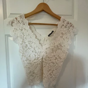 Vit spetsblus från Zara - Säljer en superfin vit spetsblus från Zara. Den är ärmlös och har ett vackert spetsmönster som ger en romantisk känsla. Perfekt för sommarens alla fester eller en mysig vårdag. Blusen är i storlek XS och sitter tight.