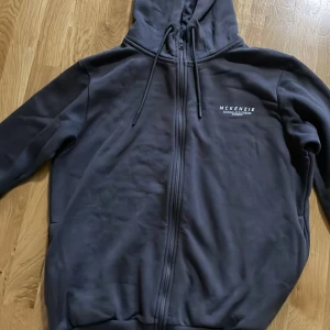Svart hoodie från McKenzie - Säljer en blå hoodie/zip från McKenzie i storlek L. Den har en dragkedja framtill och en klassisk huva med dragsko. Perfekt för en avslappnad stil och passar bra till både höst och vinter. Materialet känns mjukt och bekvämt. Väldigt bra skick inga märken eller defekter. Nytvättad 