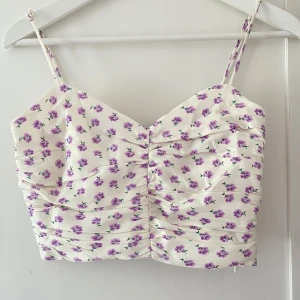 Vit blommig topp med smala axelband - Säljer en superfin vit topp med lila blommor för 150kr (ordinarie pris: 259kr). Oanvänd och med prislapp! Toppen har en rynkad design framtill och smock baktill för en bekväm passform. Materialet är siden 💘