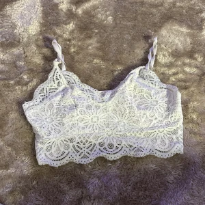 Vit spetslinne - Säljer en superfin vit spetslinne med vackra spetsdetaljer. Den är ärmlös och har justerbara axelband som är knutna för en söt look. Perfekt för sommardagar eller som ett lager under en annan topp.