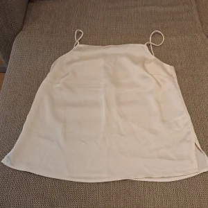 Beige linne med tunna axelband - Säljer ett stilrent beige linne med tunna axelband. Perfekt för sommardagar eller som ett lager under en kavaj. Materialet är mjukt och bekvämt, vilket gör det till ett mångsidigt plagg i garderoben.