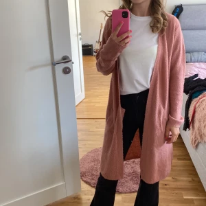Rosa lång cardigan - Säljer en superfin rosa lång cardigan som är perfekt för både vår och höst. Den är långärmad och har en mysig passform. Perfekt att slänga på sig när det är lite kyligt ute. 💖