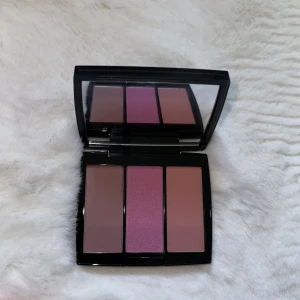 Blush Trio från Anastasia Beverly Hills - Säljer en superfin Blush Trio från Anastasia Beverly Hills i nyansen 'Pool Party'. Den innehåller tre olika färger: en mjuk lila, en rosa och en varm brunrosa. Perfekt för att skapa en fräsch och naturlig look. Kommer i en snygg svart förpackning med spegel, så den är lätt att ta med sig överallt!