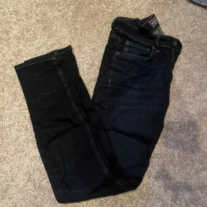 Svarta jeans från Dressmann - Snygga svarta jeans från Dressmann i klassisk stil. De har en rak passform med knapp och dragkedja i gylfen. Perfekta för en stilren look.