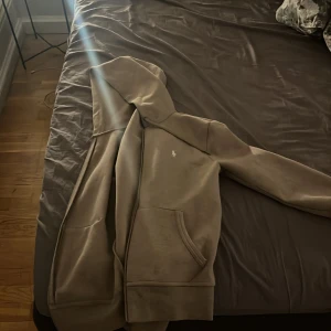 Beige hoodie från Ralph Lauren - Säljer en stilren beige hoodie från Ralph Lauren. Den har en klassisk design med en liten broderad logotyp på bröstet och en bekväm huva. Perfekt för en avslappnad look.