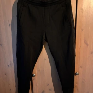 Svarta mjukisbyxor från Emporio Armani - Snygga svarta mjukisbyxor från Emporio Armani med broderad logga längs sidan. Byxorna har en bekväm passform och är perfekta för en avslappnad stil. De har elastisk midja och praktiska fickor. Köpt på Nordlunds i Växjö för 2999. Aldrig använda. Storlek S men passar M