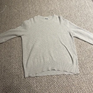 Grå stickad tröja från Zara - Säljer en stilren beige stickad tröja från Zara. Tröjan har en klassisk rund hals och långa ärmar, perfekt för kyligare dagar. Den är mjuk och bekväm, idealisk för både vardag och avslappnade tillfällen. Storlek L sitter mer som M, vid minsta fundering är det bara att höra av sig. 