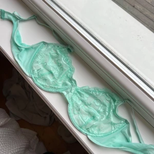 Mintgrön spets-bh - Säljer en vacker mintgrön bh med spetsdetaljer. Den har en elegant design med genomskinliga partier och justerbara axelband för perfekt passform. Perfekt för att känna sig extra fin. Självklart oanvänt 