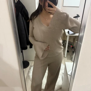Beige ribbad sett - Säljer en stilren beige ribbad sett med v-ringning och långa ärmar. Tröjan har en loose passform och vida ärmslut som ger en trendig look. Perfekt för en avslappnad stil.