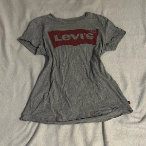 Grå t-shirt från Levi's - Säljer en grå t-shirt från Levi's med det klassiska röda logotyptrycket på bröstet. T-shirten är kortärmad och tillverkad i mjuk bomull. Perfekt för en avslappnad stil.