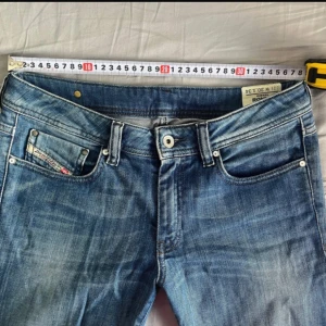 Blå jeans från Diesel - Snygga blå jeans från Diesel med en klassisk femficksdesign och diskreta slitningar för en trendig look. Jeansen har en knappgylf och bälteshällor, vilket gör dem perfekta för en avslappnad stil. Jag har klippt på ena sidan för att dom är väldigt långa!!