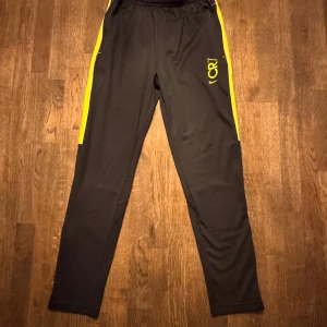 Svarta träningsbyxor Nike CR7 - Svarta Nike CR7 byxor med dragkedja längs vaderna i storlek L barnstorlek (147-158 cm) varan har använts lite men är fortfarande i väldigt bra skick.
